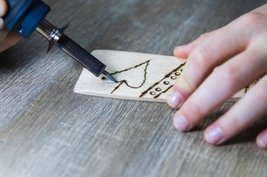 Bir çocuk eli ahşap bir tabağa odun yakma ve pirografik süslemelerle çizer.