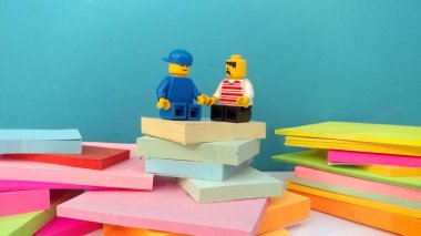 Duvarın yanında elinde not kağıtlarıyla oturan iki lego adam.