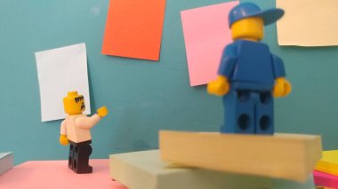 Duvarın yanında elinde post-it olan iki lego adam.