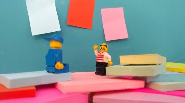 Duvarın yanında elinde post-it olan iki lego adam.