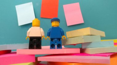 Duvarın yanında elinde post-it olan iki lego adam.