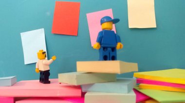 Duvarın yanında elinde post-it olan iki lego adam.