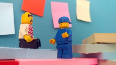 Duvarın yanında elinde post-it olan iki lego adam.