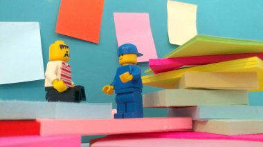 Duvarın yanında elinde post-it olan iki lego adam.