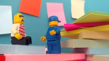 Duvarın yanında elinde post-it olan iki lego adam.