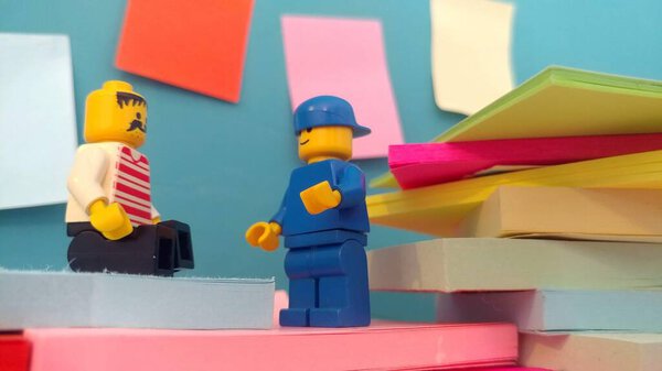 Two Lego men standing near a wall with post-its