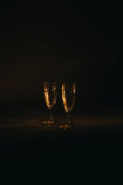 İki şarap kadehi koyu arkaplanda turuncu ışıkla aydınlatılır. Kompozisyonun silueti ve geometrisi. Metin için boşluk