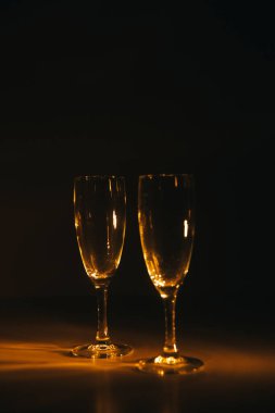 İki şarap kadehi koyu arkaplanda turuncu ışıkla aydınlatılır. Kompozisyonun silueti ve geometrisi. Metin için boşluk