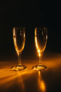 İki şarap kadehi koyu arkaplanda turuncu ışıkla aydınlatılır. Kompozisyonun silueti ve geometrisi. Metin için boşluk