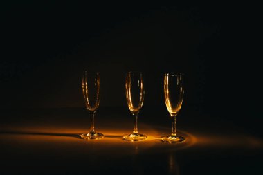Birkaç şampanya kadehinden oluşan bir grup, koyu bir arka plan karşısında güzelce aydınlatılıyor. Şenlikli bir kompozisyon. Metin için boşluk
