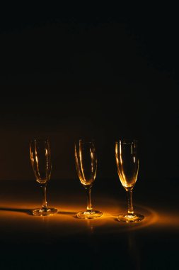 Birkaç şampanya kadehinden oluşan bir grup, koyu bir arka plan karşısında güzelce aydınlatılıyor. Şenlikli bir kompozisyon. Metin için boşluk