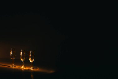 Birkaç şampanya kadehinden oluşan bir grup, koyu bir arka plan karşısında güzelce aydınlatılıyor. Şenlikli bir kompozisyon. Metin için boşluk