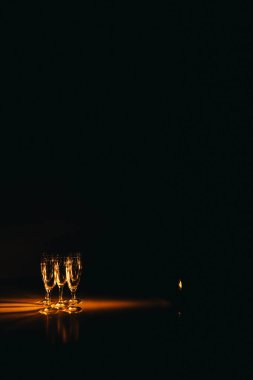 Birkaç şampanya kadehinden oluşan bir grup, koyu bir arka plan karşısında güzelce aydınlatılıyor. Şenlikli bir kompozisyon. Metin için boşluk