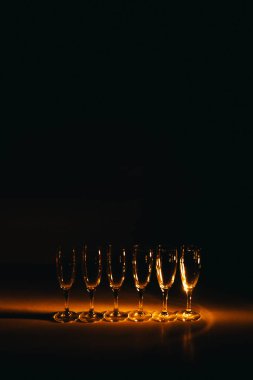 Birkaç şampanya kadehinden oluşan bir grup, koyu bir arka plan karşısında güzelce aydınlatılıyor. Şenlikli bir kompozisyon. Metin için boşluk