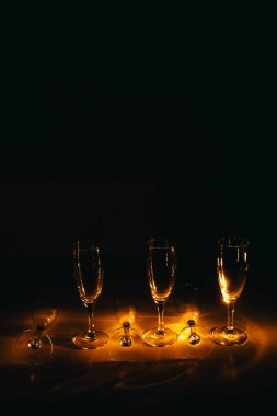 Birkaç şampanya kadehinden oluşan bir grup, koyu bir arka plan karşısında güzelce aydınlatılıyor. Şenlikli bir kompozisyon. Metin için boşluk