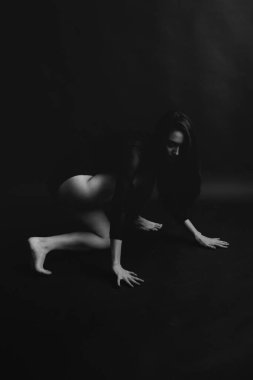 Şık ve modaya uygun bir fotoğraf, siyah beyaz bir beden giymiş bir kızın portresi. Kız özgürce dans ediyor ve stüdyoda karanlık bir arkaplanda kameranın önünde poz veriyor.