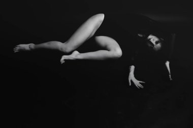 Şık ve modaya uygun bir fotoğraf, siyah beyaz bir beden giymiş bir kızın portresi. Kız özgürce dans ediyor ve stüdyoda karanlık bir arkaplanda kameranın önünde poz veriyor.