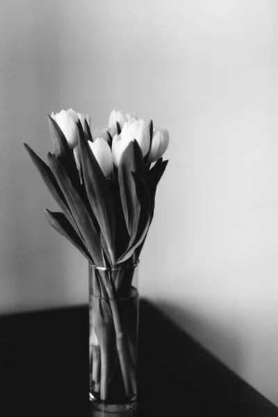 Black and white photo of a bouquet of white tulips in a glass vase with water