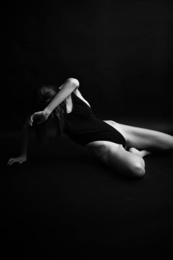Siyah, beyaz, otantik, ince bir dansçının siyah bir vücut giysisi içindeki fotoğrafı. Stüdyo yazarının fotoğrafı. sıra dışı minimalist pozlar