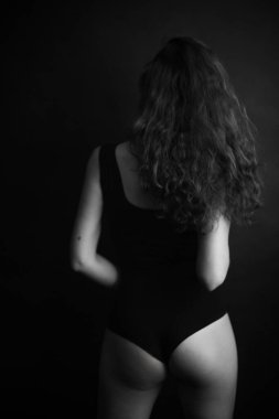  Moda bir stüdyo minimalist fotoğrafı, siyah elbiseli kıvırcık saçlı bir kız güzel poz veriyor ve ince vücudunu gösteriyor.