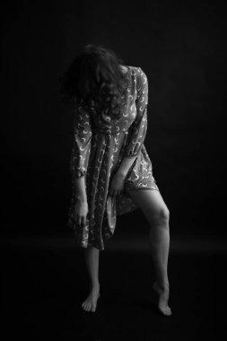Curly-haired girl in a feminine dress, black and white studio portrait, fashion and art