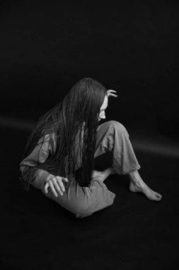 Siyah-beyaz stüdyo fotoğrafı, kot pantolon ve kazak giyen genç bir kız kamera önünde afroko pozlar veriyor.