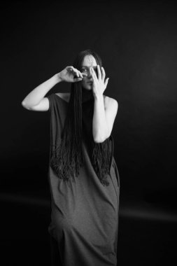 Siyah-beyaz Stüdyo fotoğrafı, uzun siyah elbiseli, afro örgülü, bitkilerle poz veren genç bir kız.