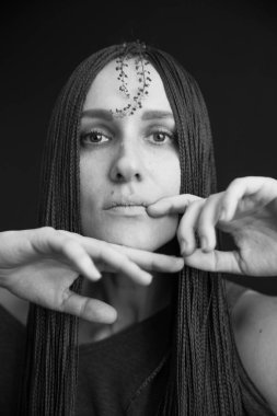 Siyah-beyaz Stüdyo fotoğrafı, uzun siyah elbiseli, afro örgülü, bitkilerle poz veren genç bir kız.