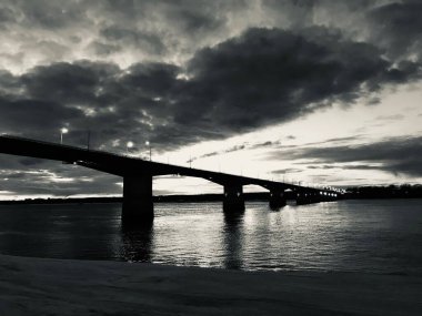 Nehir üzerindeki bir köprünün siyah beyaz fotoğrafı, karanlık şehir manzarası.