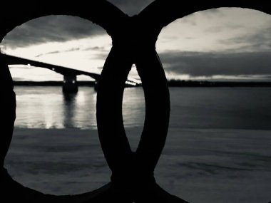 Nehir üzerindeki bir köprünün siyah beyaz fotoğrafı, karanlık şehir manzarası.