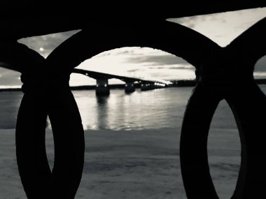 Nehir üzerindeki bir köprünün siyah beyaz fotoğrafı, karanlık şehir manzarası.