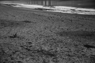 Okyanustaki yüksek ve alçak gelgitten sonra kumlu sahildeki desenler, siyah ve beyaz soyut kum arka planı