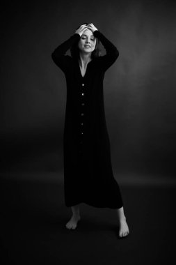 Esmer bir kadının uzun siyah elbiseli portresi karanlık bir stüdyo arka planında, sanat ve moda fotoğrafçılığında.