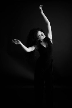 Kıvırcık bir esmerin basit ve şık portresi, kameraya ücretsiz poz, siyah yumuşak odak