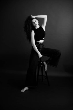 Kıvırcık bir esmerin basit ve şık portresi, kameraya ücretsiz poz, siyah yumuşak odak