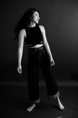 Kıvırcık bir esmerin basit ve şık portresi, kameraya ücretsiz poz, siyah yumuşak odak