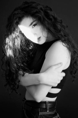 Kıvırcık bir esmerin basit ve şık portresi, kameraya ücretsiz poz, siyah yumuşak odak