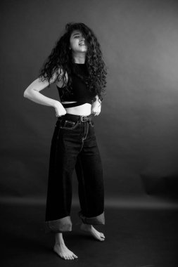 Kıvırcık bir esmerin basit ve şık portresi, kameraya ücretsiz poz, siyah yumuşak odak