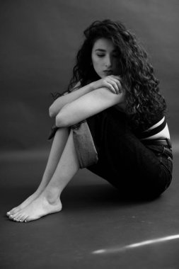 Kıvırcık bir esmerin basit ve şık portresi, kameraya ücretsiz poz, siyah yumuşak odak