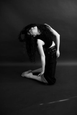 Kıvırcık bir esmerin basit ve şık portresi, kameraya ücretsiz poz, siyah yumuşak odak