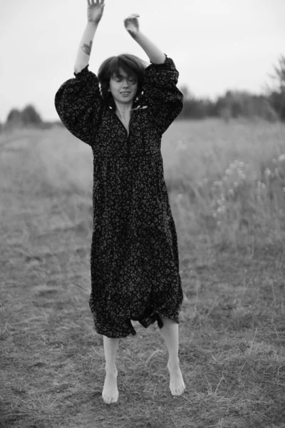 Bir kız tarlada yürüyor, siyah-beyaz bir yaz fotoğrafı, uzun bir elbise içinde doğa yürüyüşü.