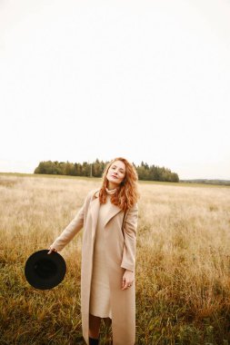 Sonbahar portresi, siyah şapkalı kızıl saçlı bir kız ve doğada yürüyen kahverengi bir ceket. Doğal yerlerdeki güzel portre, bulanık arkaplan ve bulanık odak