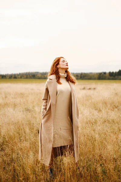 Doğada sonbahar montu giymiş kızıl saçlı bir kızın portresi, arka plan bulanık ve bir film kamerasında bulanık görüntü.