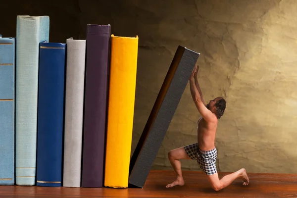 Mann stützt fallendes Buch im Bücherregal — Stockfoto