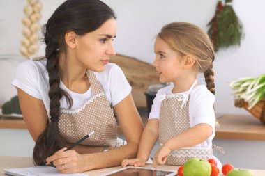 Mutfakta mutlu bir aile. Anne ve kız çocuk mutfakta lezzetli kahvaltı hazırlamak için menü hazırlıyorlar. Küçük yardımcı ev işi için hazır.