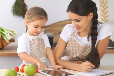 Mutfakta mutlu bir aile. Anne ve kız çocuk mutfakta lezzetli kahvaltı hazırlamak için menü hazırlıyorlar. Küçük yardımcı ev işi için hazır.