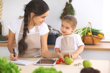 Mutfakta mutlu bir aile. Anne ve kız çocuk mutfakta lezzetli kahvaltı hazırlamak için menü hazırlıyorlar. Küçük yardımcı ev işi için hazır.