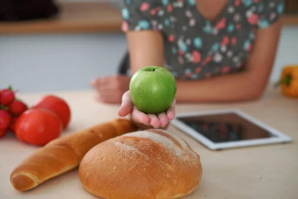 Primo piano della mano femminile che tiene mela verde negli interni della cucina. Molte verdure e altri pasti a tavola di vetro sono pronti per essere cucinati presto. — Foto Stock