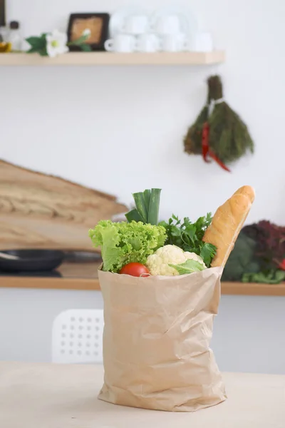 Paper bag full of vegetables on the table in kitchen interiors. Healthy meal and vegetarian concept