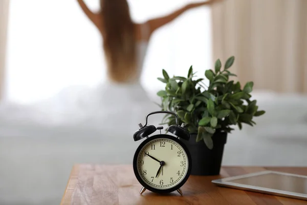Alarm clock standing on bedside table has already rung early morning to wake up woman in bed sitting in background. Early awakening, not getting enough sleep, oversleep, time line concept — Stock Fotó